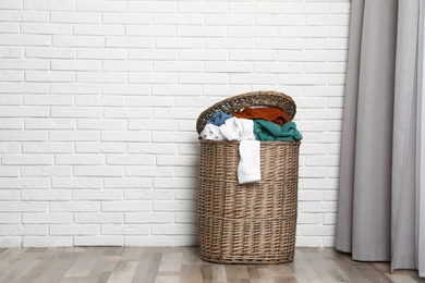 Wicker laundry basket full of dirty clothes near brick wall in room. Space for text