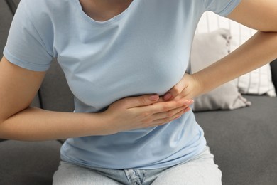 Photo of Woman suffering from stomach pain on sofa indoors, closeup