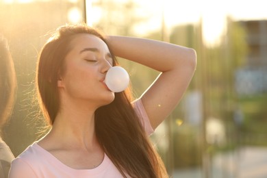 Photo of Beautiful young woman blowing bubble gum outdoors on sunny day. Space for text