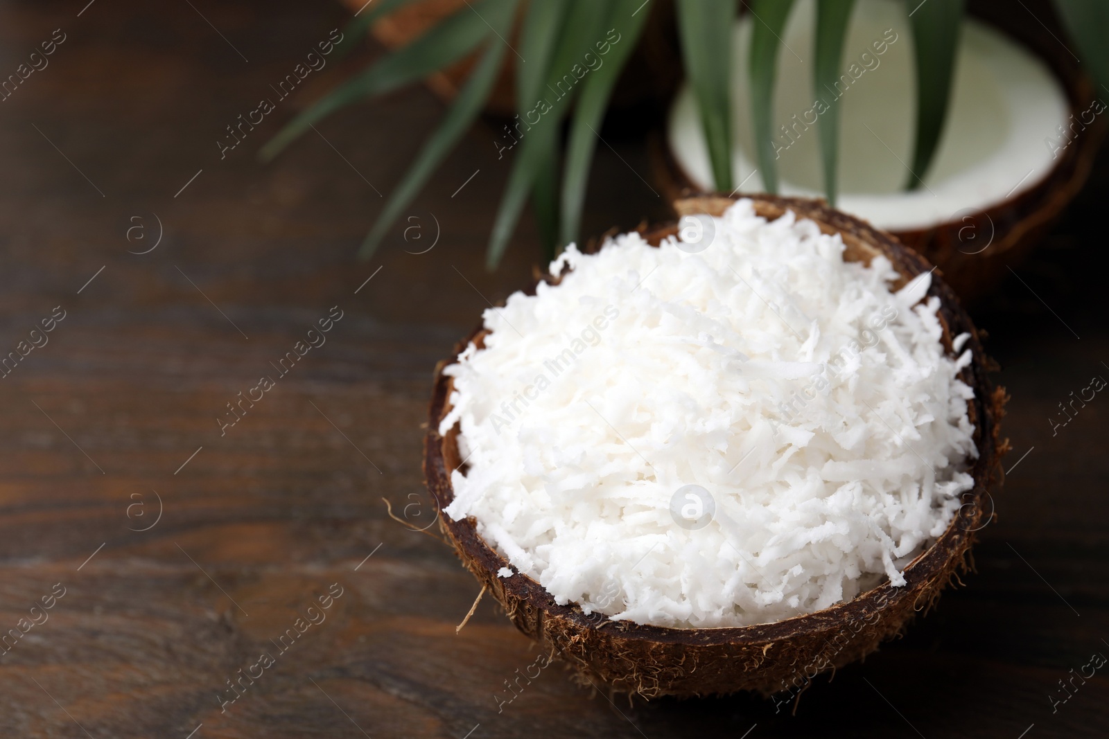 Photo of Coconut flakes in nut shell on wooden table, space for text