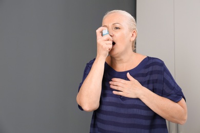 Photo of Woman using asthma inhaler indoors with space for text