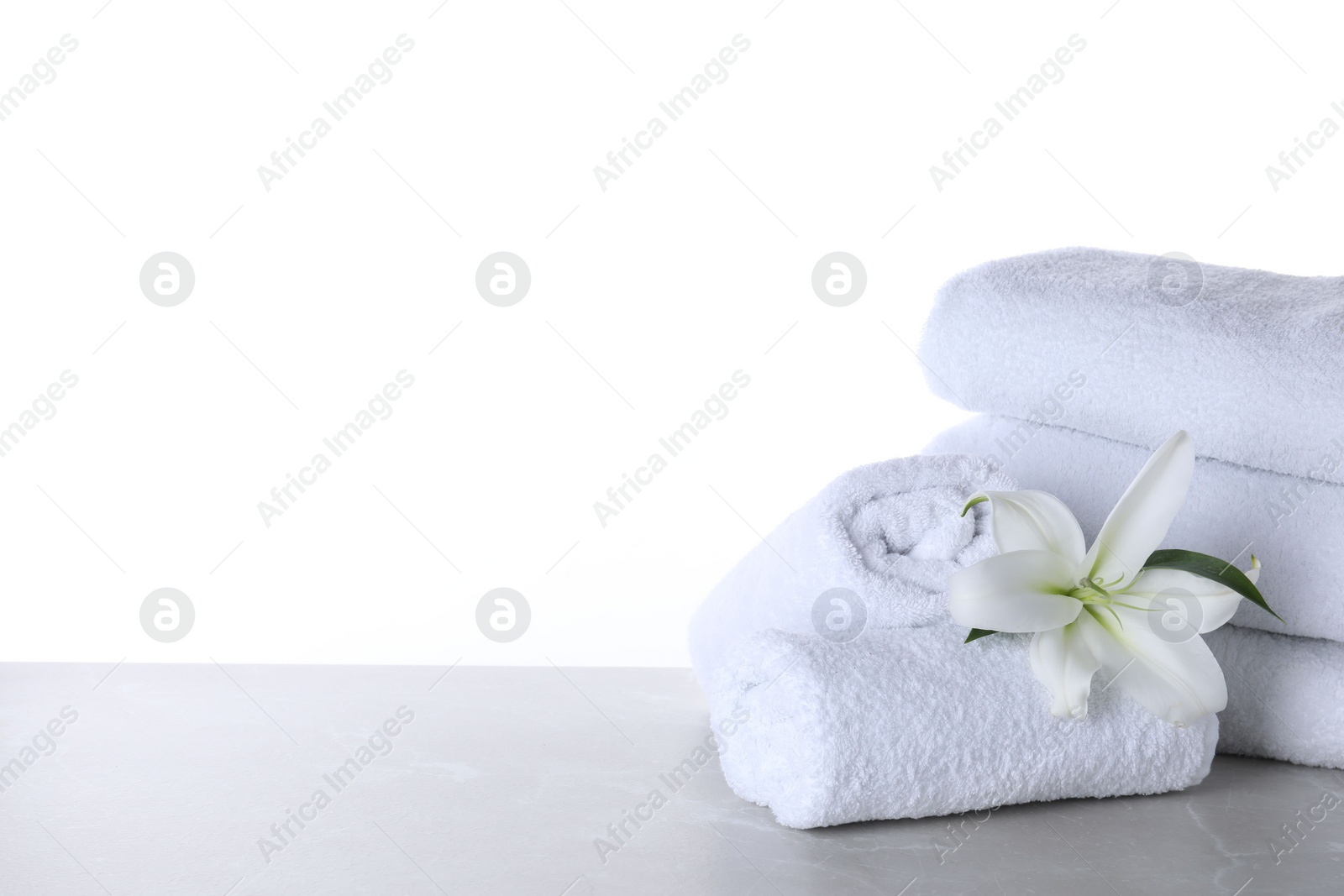 Photo of Fresh towels and lily flower on light grey marble table against white background. Space for text