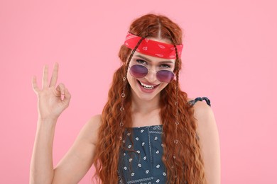 Photo of Stylish young hippie woman in sunglasses showing OK gesture on pink background