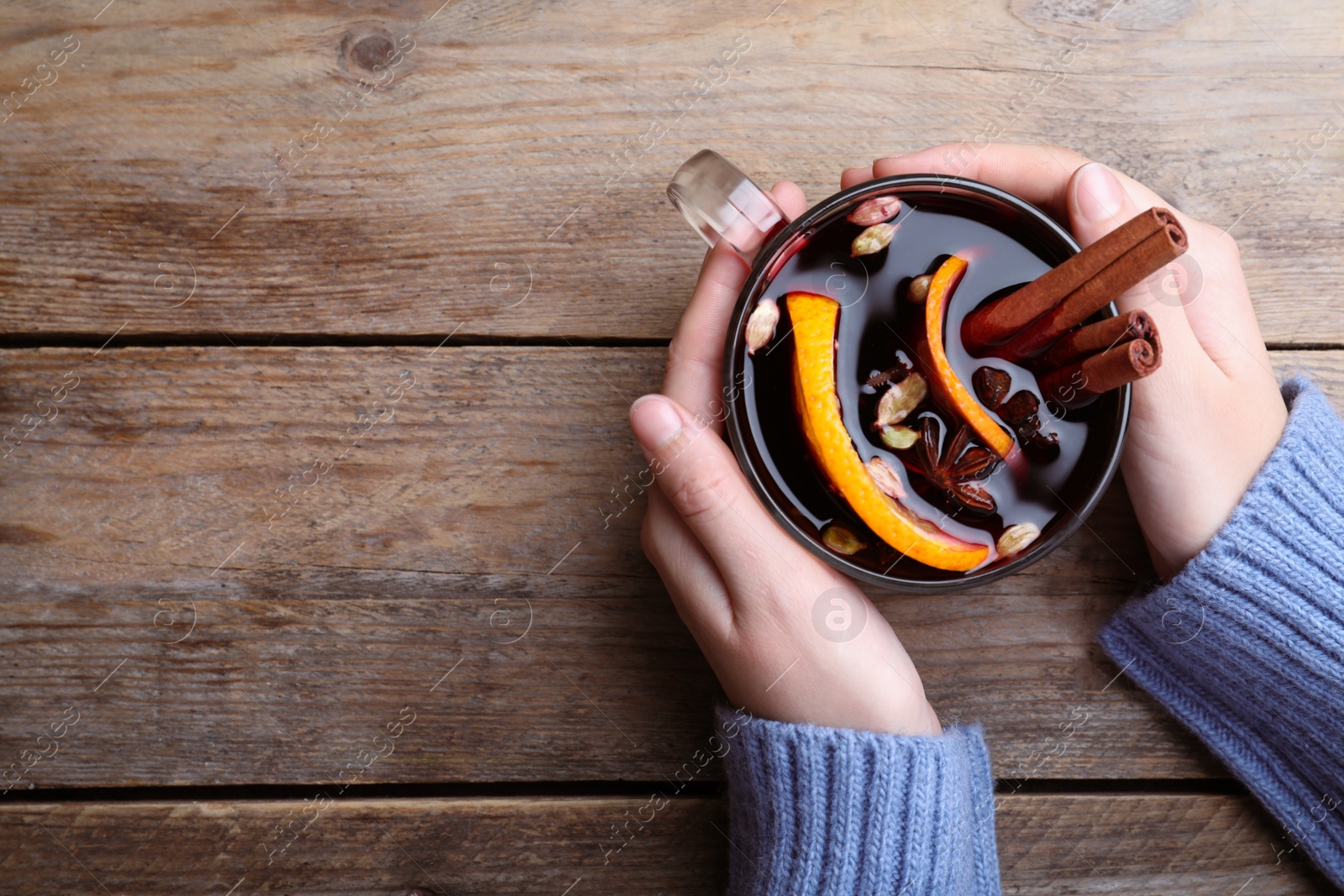 Photo of Woman with cup of mulled wine at wooden table, top view. Space for text