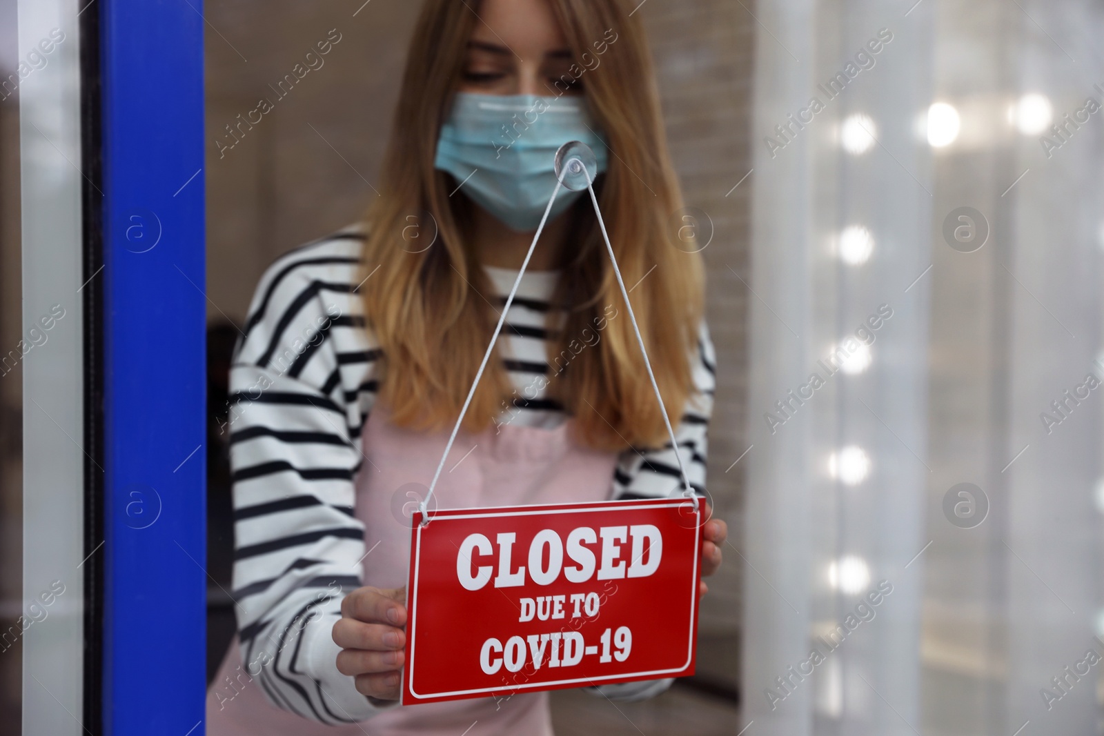 Photo of Business owner in mask hanging red sign with text Closed Due To Covid-19 onto glass door. Coronavirus quarantine