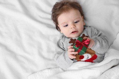 Photo of Cute little baby with gift on soft bed, top view. Space for text