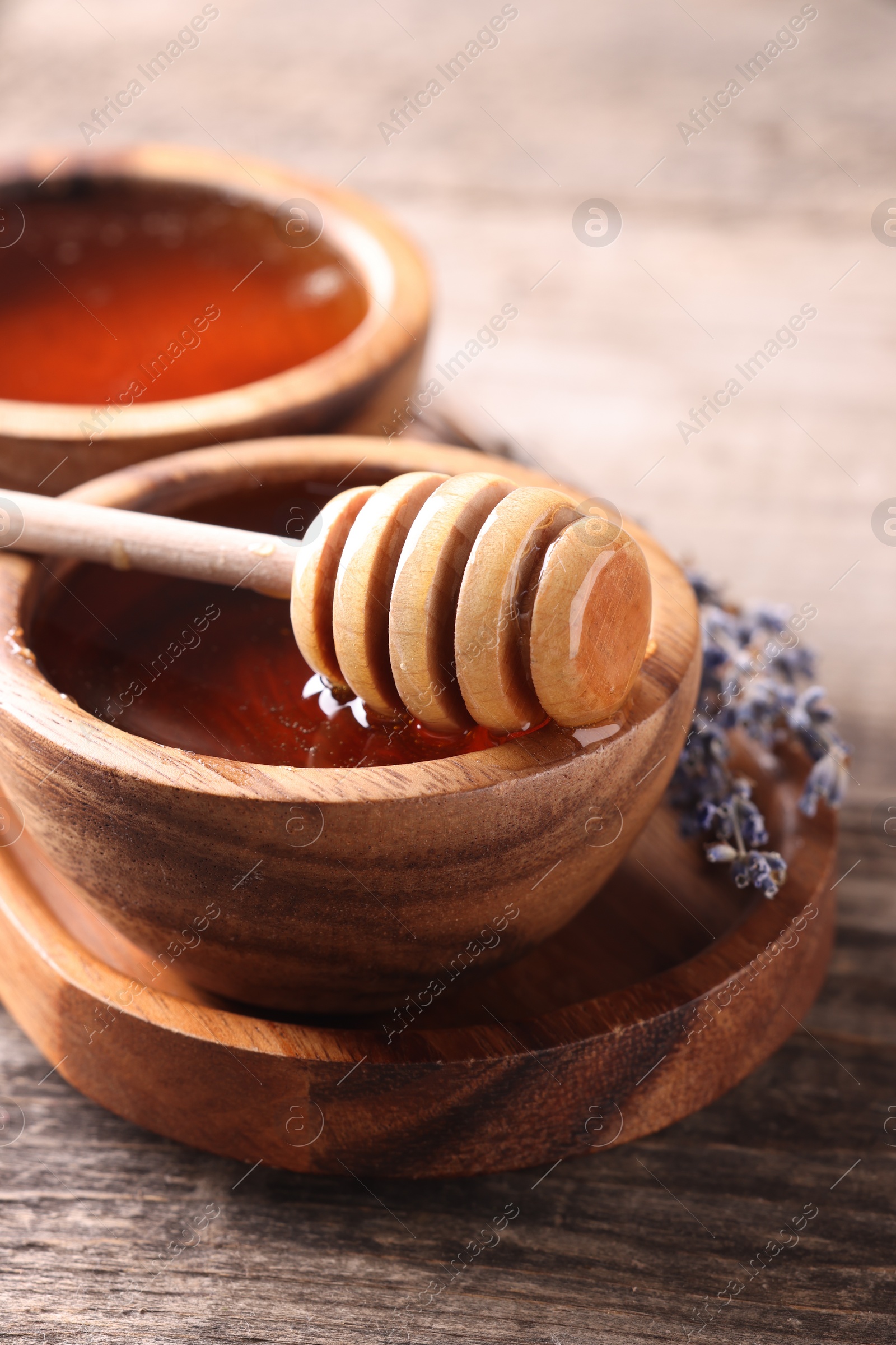 Photo of Delicious honey in bowls, lavender flowers and dipper on wooden table, closeup