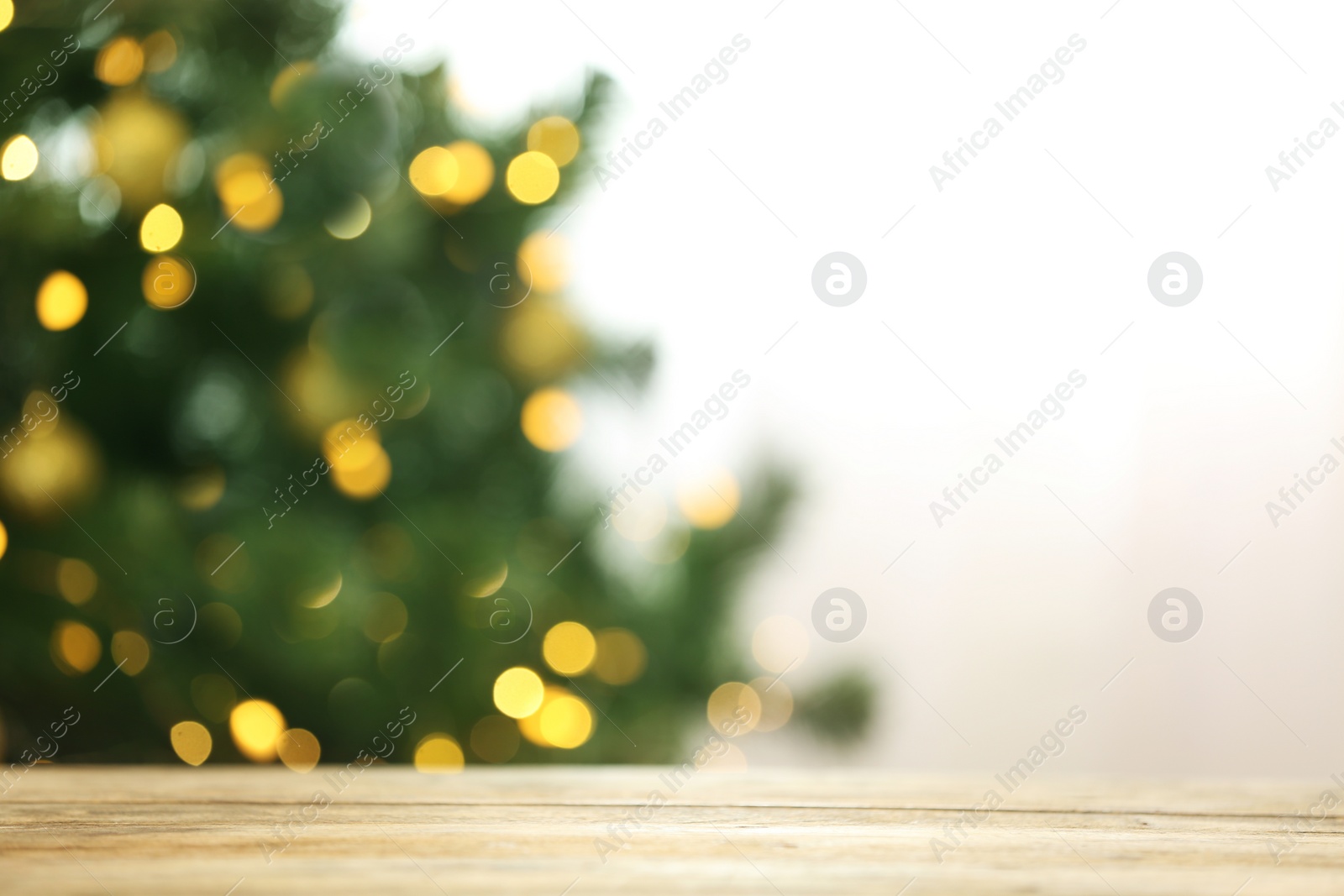 Photo of Blurred view of fir tree with glowing Christmas lights near table indoors. Festive mood