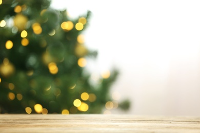 Photo of Blurred view of fir tree with glowing Christmas lights near table indoors. Festive mood