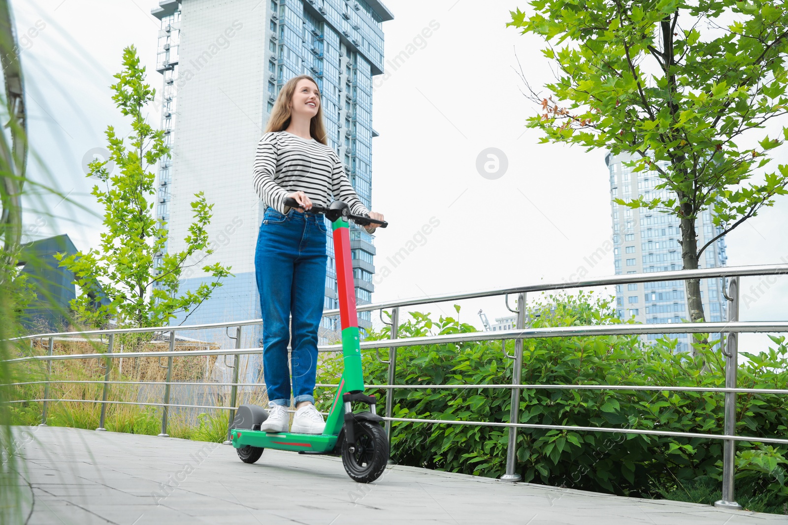 Photo of Happy woman riding modern electric kick scooter on city street, space for text