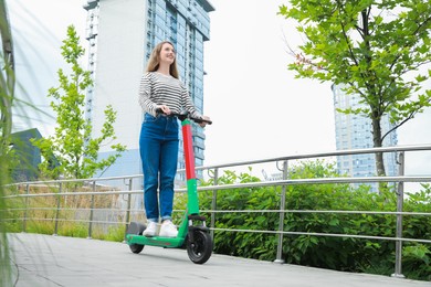 Happy woman riding modern electric kick scooter on city street, space for text