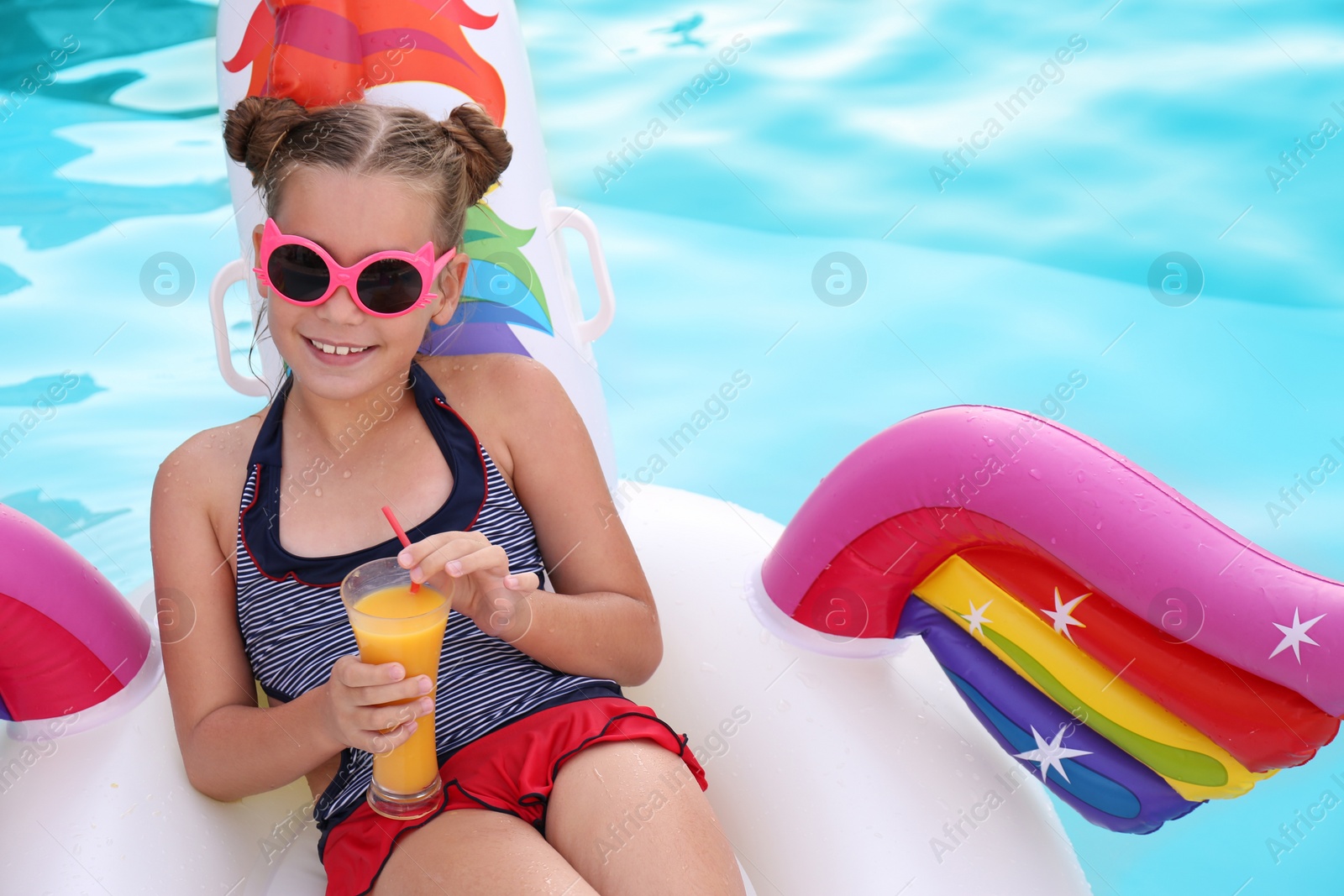 Photo of Happy girl with drink on inflatable unicorn in swimming pool