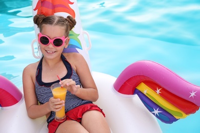 Happy girl with drink on inflatable unicorn in swimming pool