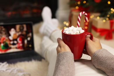 Photo of Woman drinking delicious cocoa and watching Christmas movie at home, closeup. Space for text