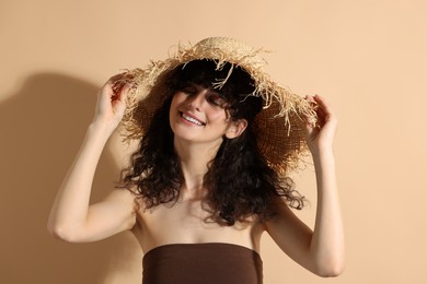 Photo of Beautiful happy woman wearing straw hat in sunlight on beige background. Sun protection accessory