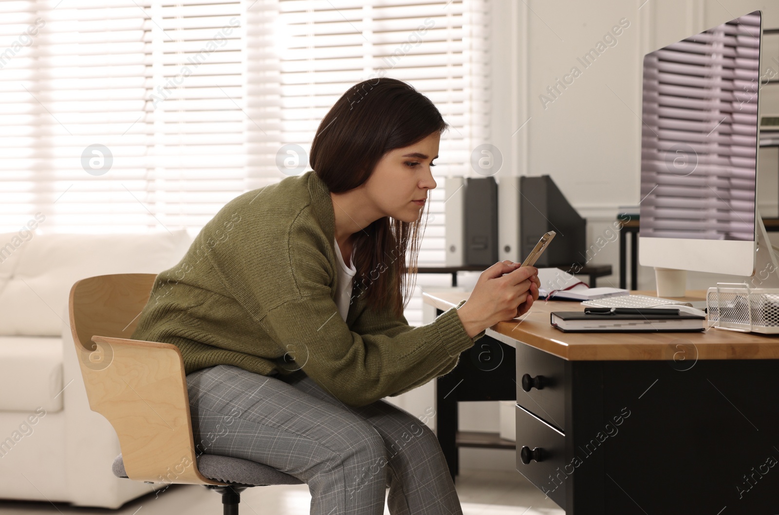 Photo of Young woman with bad posture using smartphone in office