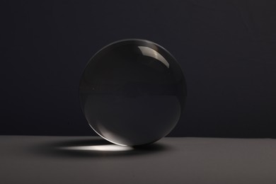 Photo of Transparent glass ball on table against dark background