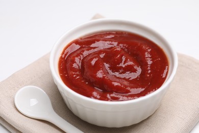 Organic ketchup in bowl and spoon on white table, closeup. Tomato sauce