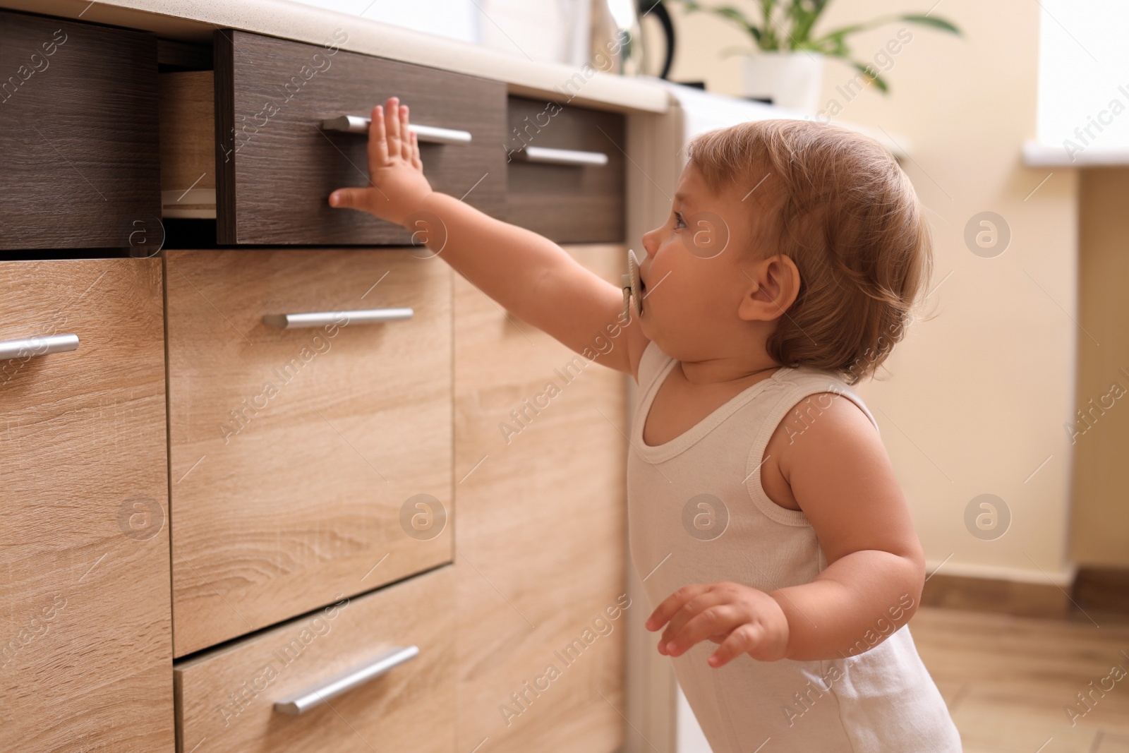 Photo of Little child exploring drawer indoors. Dangerous situation