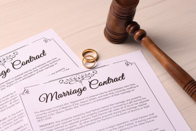 Marriage contracts, gold rings and gavel on light wooden table, closeup