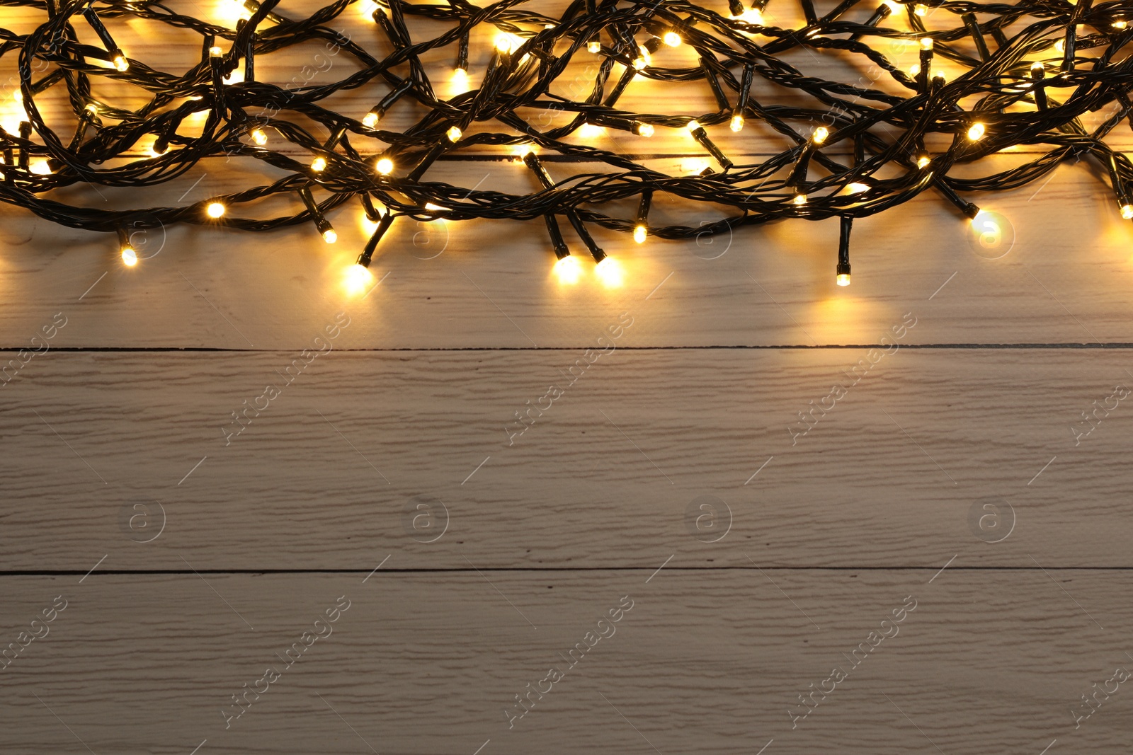 Photo of Glowing festive lights on wooden background, top view. Space for text