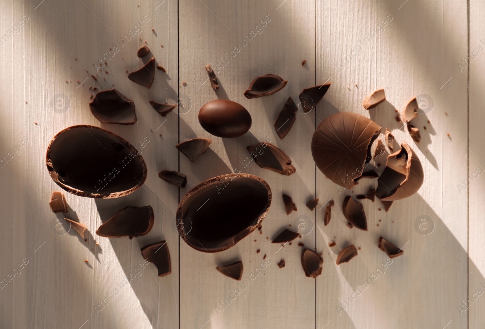 Photo of Broken and whole chocolate eggs on white wooden table, flat lay