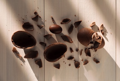 Photo of Broken and whole chocolate eggs on white wooden table, flat lay