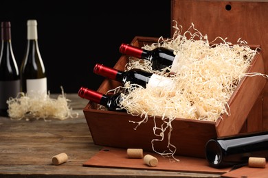 Photo of Box with wine bottles on wooden table against black background