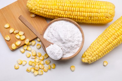 Photo of Bowl with corn starch, ripe cobs and kernels on white marble table, flat lay