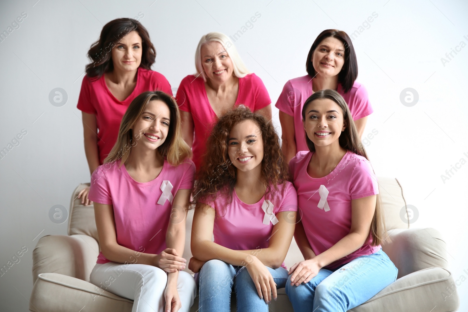 Photo of Group of women with silk ribbons on sofa near light wall. Breast cancer awareness concept