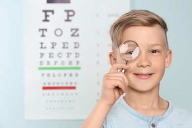 Photo of Cute little boy with magnifier in ophthalmologist office