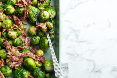 Photo of Delicious Brussels sprouts with bacon on white marble table, top view. Space for text