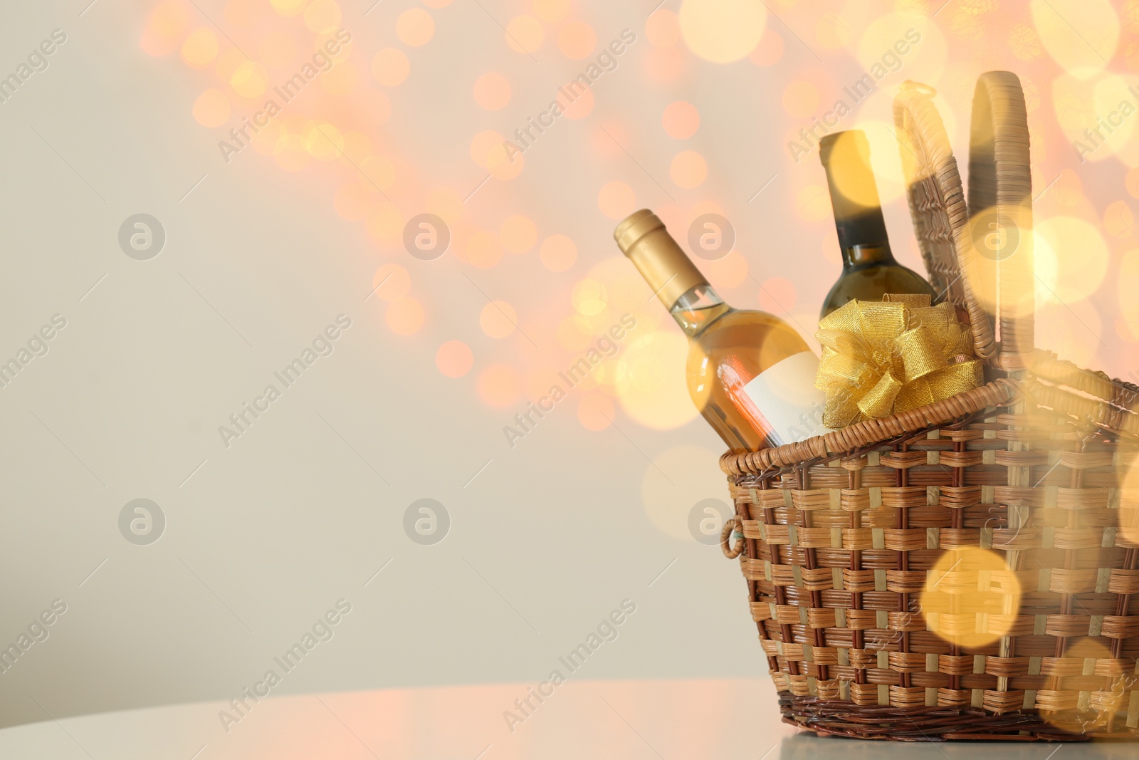 Photo of Wicker basket with bottles of wine against blurred lights. Space for text