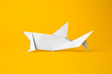 Photo of Origami art. Handmade white paper shark on yellow background