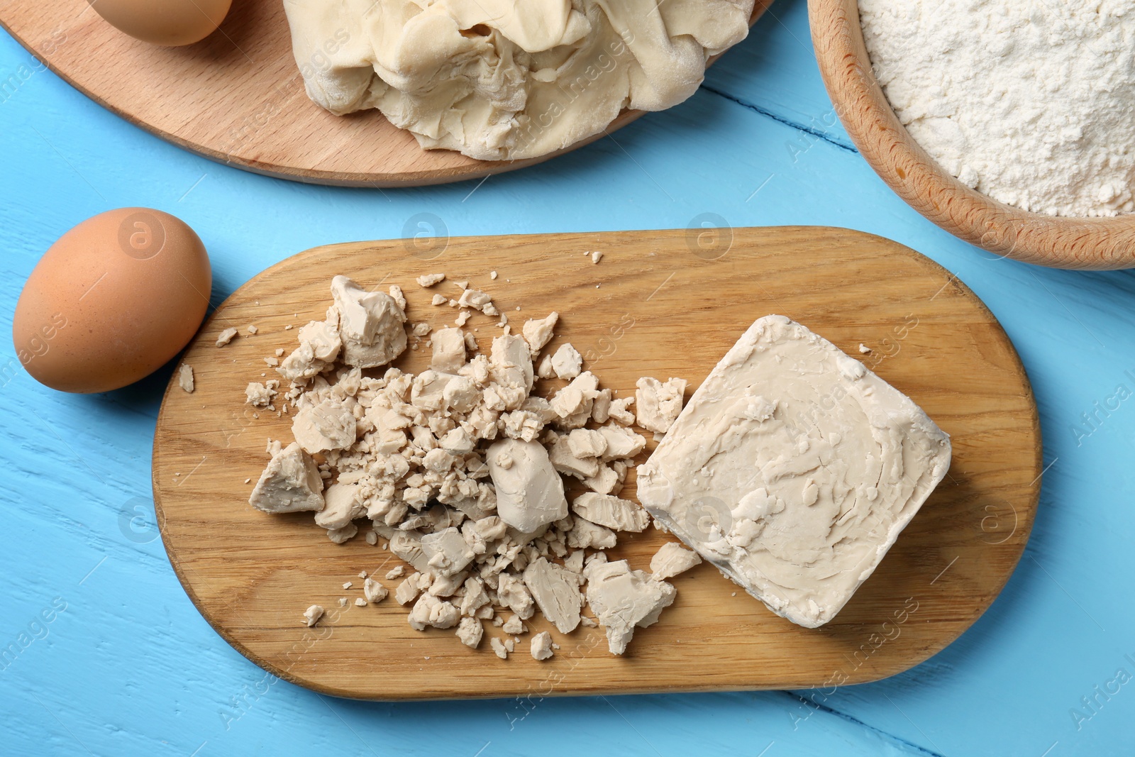 Photo of Pieces of compressed yeast, eggs, dough and flour on light blue wooden table, flat lay