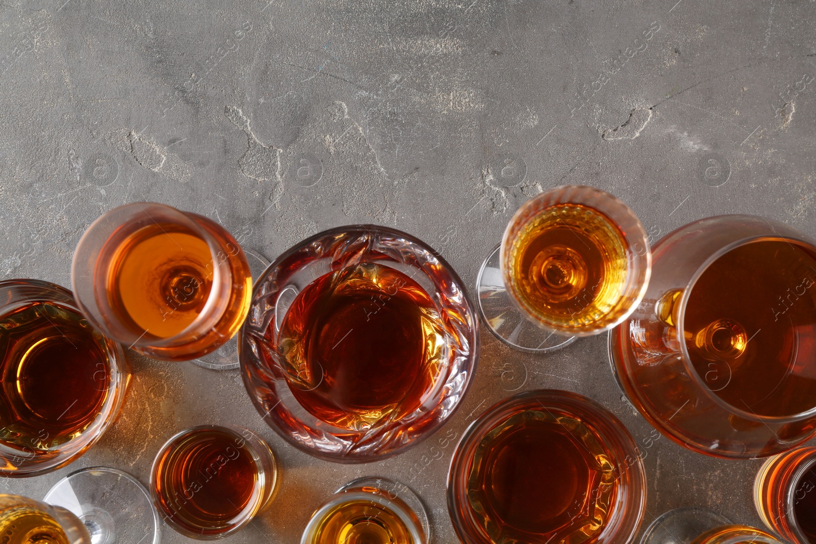 Photo of Different delicious liqueurs in glasses on grey table, flat lay