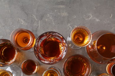 Different delicious liqueurs in glasses on grey table, flat lay