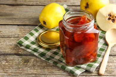 Photo of Tasty homemade quince jam in jar, spoon and fruits on wooden table, closeup. Space for text
