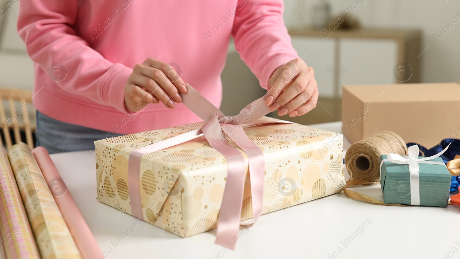 Photo of Woman wrapping gift at white table indoors, closeup