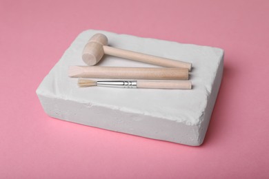 Photo of Educational toy for motor skills development. Excavation kit (plaster, digging tools and brush) on pink background, closeup