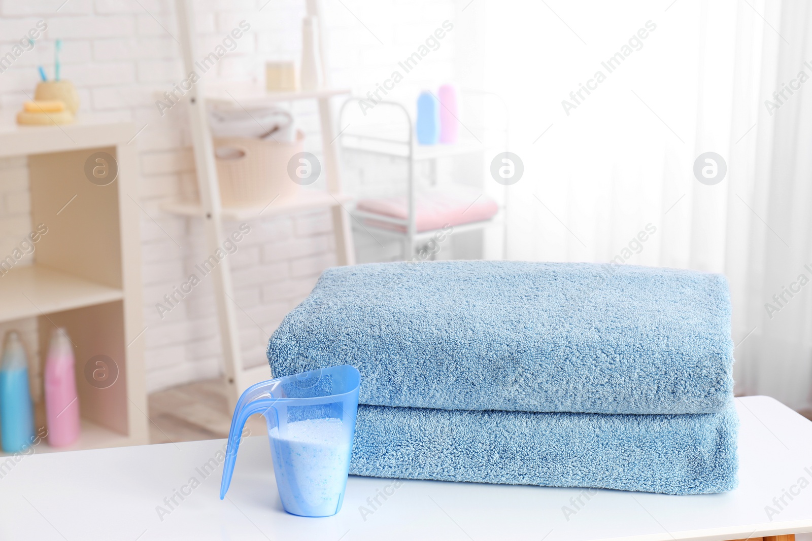 Photo of Measuring cup with washing powder and clean towels on table indoors. Laundry day