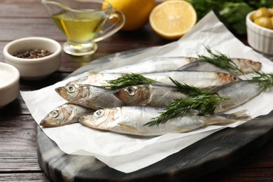 Photo of Fresh raw sprats, dill and other products on wooden table, closeup