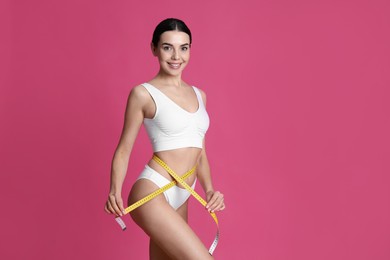 Photo of Young woman measuring waist with tape on pink background. Space for text