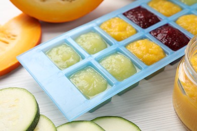 Photo of Different purees in ice cube tray and ingredients on white table, closeup. Ready for freezing