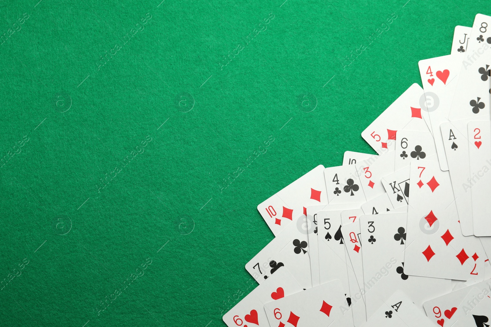 Photo of Scattered playing cards on green table, top view. Space for text