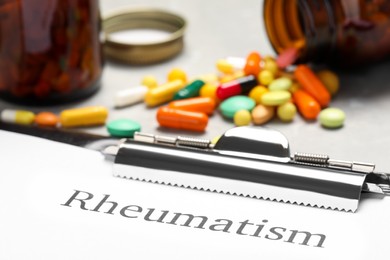 Photo of Clipboard with word Rheumatism and pills on table, closeup