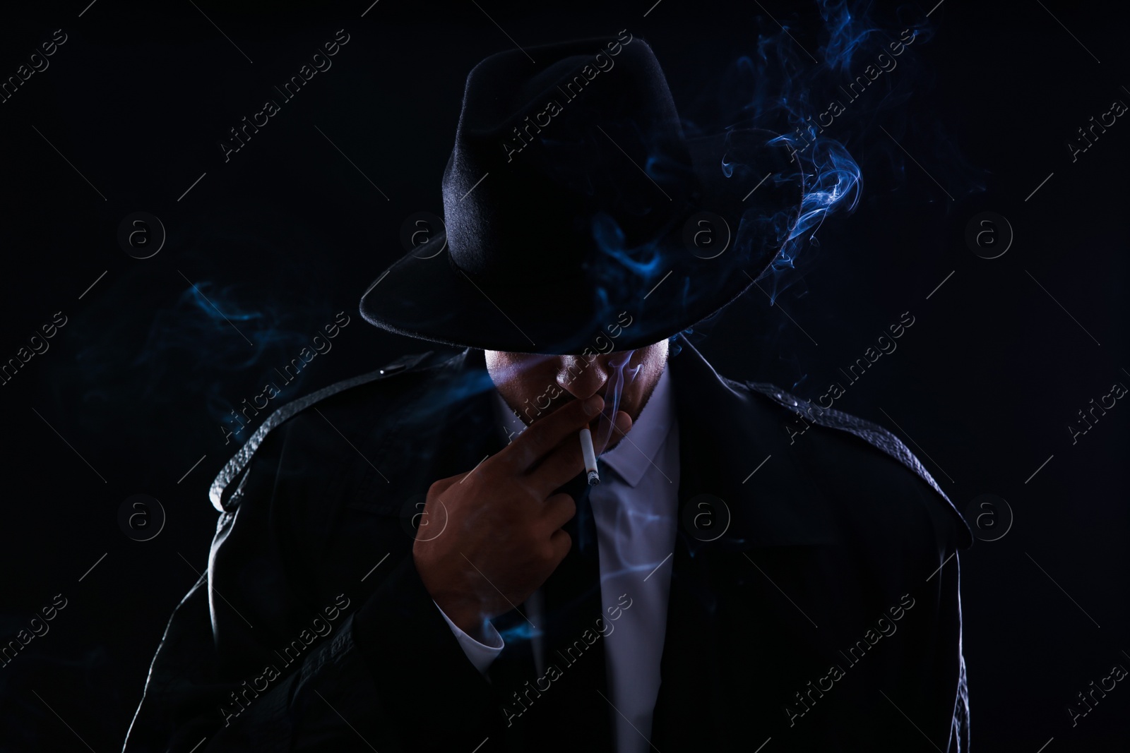 Photo of Old fashioned detective smoking cigarette on dark background