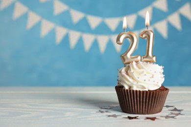Photo of Coming of age party - 21th birthday. Delicious cupcake with number shaped candles on white wooden table, space for text