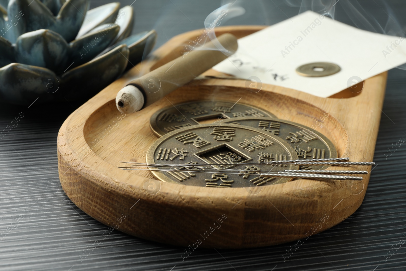 Photo of Acupuncture needles, moxa stick and antique Chinese coins on wooden table, closeup