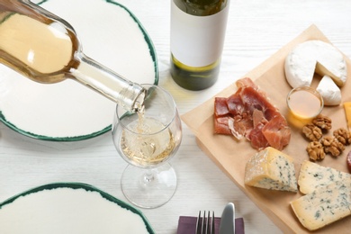 Photo of Pouring white wine into glass on table with delicious food